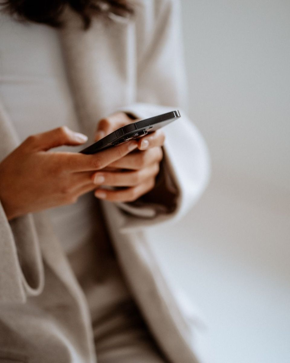 Close-up of a person in a soft beige coat holding a phone with both hands